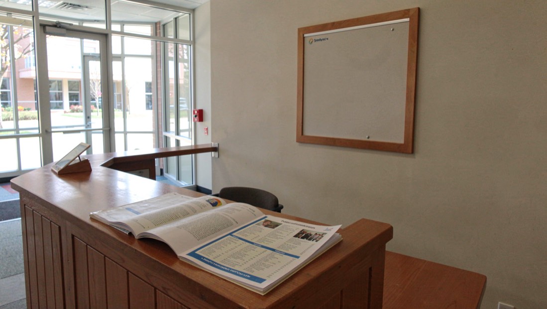 A public information desk with a printed services directory and a wall sign board behind it